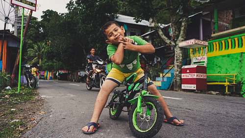 bike boy riding black and green bike near man riding motorcycle at daytime vehicle