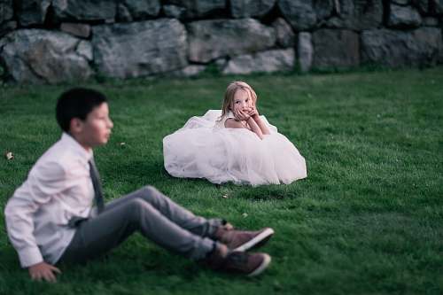 person girl sitting on green grass looking at the boy sitting on green grass human