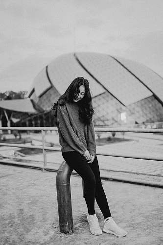 person grayscale photo of woman sitting on metal bar black-and-white