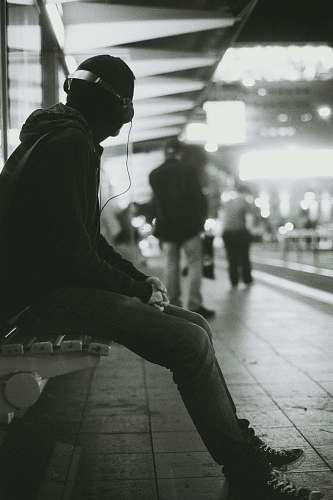 human grayscale photography of a man sitting on bench while listening music person