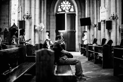 human grayscale photography of man sitting on pew black-and-white