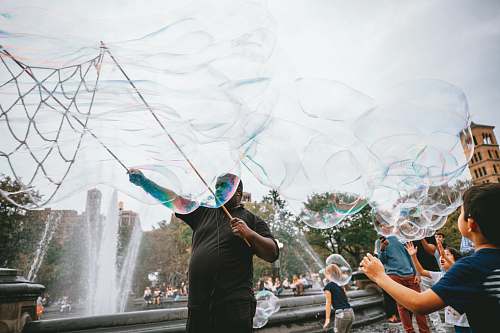 human man and boy performing bubble artworks near fountain at daytime bubble
