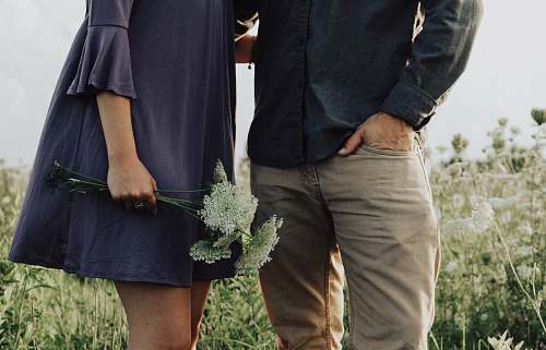 human man and woman standing on white flower field at daytime person