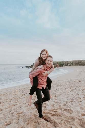 human man carrying woman beside seashore person