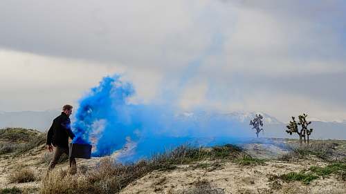 person man holding black box with blue smoke walking on grass field during daytime human