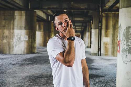 human man in white crew-neck t-shirt standing near gray concrete pillar person