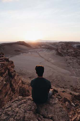 person man sitting on cliff facing open field during daytime human