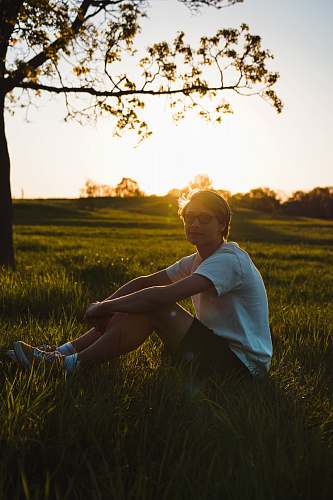 human man sitting on grass while resting hand on knee during golden hour person