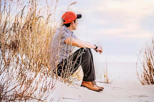 human man sitting on sand with wheat looking right during daytime person