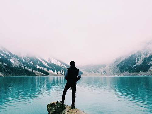person man standing on brown rock facing beside body of water human