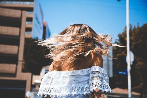 person photo of woman wearing white off-shoulder crop top standing beside concrete building under clear blue sky human
