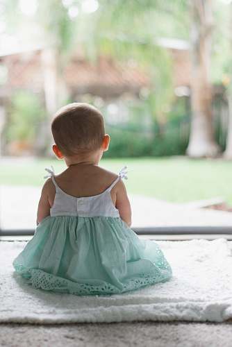human selective focus photo of toddler wearing sleeveless dress sitting on floor baby