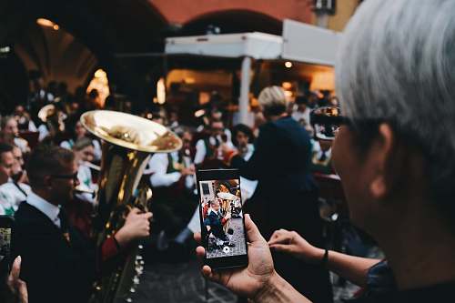 human selective focus photo of woman holding phone taking a photo of man playing instrument person