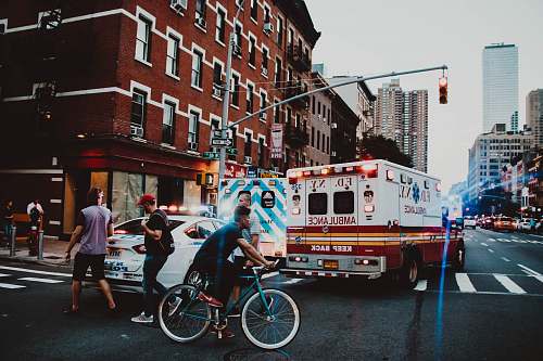 person three people walking near man riding bicycle on street near ambulance human