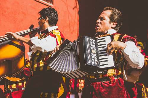 human two men playing cello and accordion beside red building photo music
