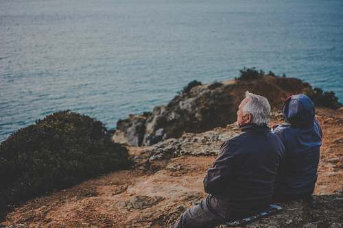 person two person sitting on rock staring at body of water during daytime human