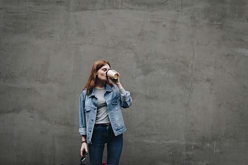 human woman drinking on mug near gray wall during daytime person