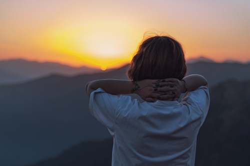 human woman facing backward holding head facing sunset person
