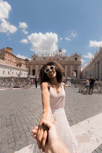 person woman holding person's hand near buildings under white and blue cloudy sky human