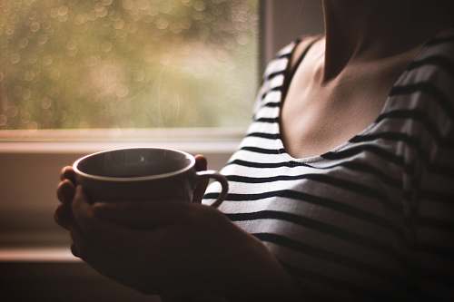 person woman in black and white striped top holding white ceramic mug cup