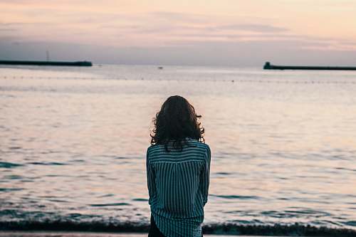 human woman in front ocean water under white sky back