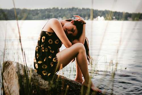 human woman sitting on rock near water person