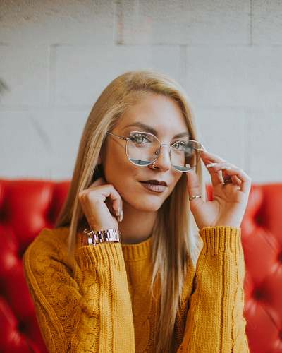 person woman sitting on tufted red sofa while holding gray framed eyeglasses human