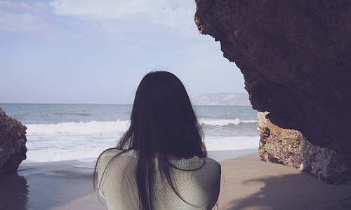 human woman sitting under rock facing sea person