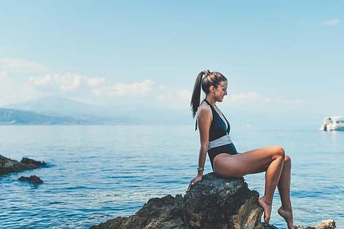 human woman wearing monokini sitting on brown rock near shore person