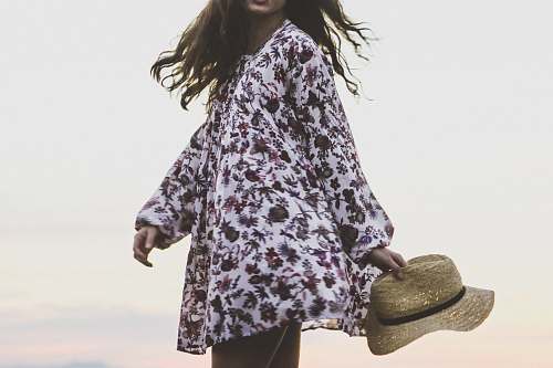 human woman wearing white and brown floral long-sleeved shirt while holding brown fedora hat person