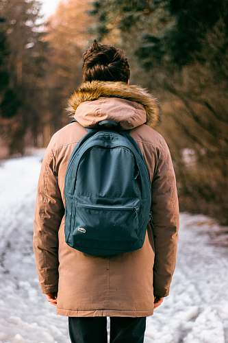 people back photo of woman wearing brown parka hoodie and green backpack on snow human