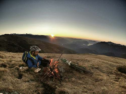 people man laying on brown grass infront of bonefire during sunrise human