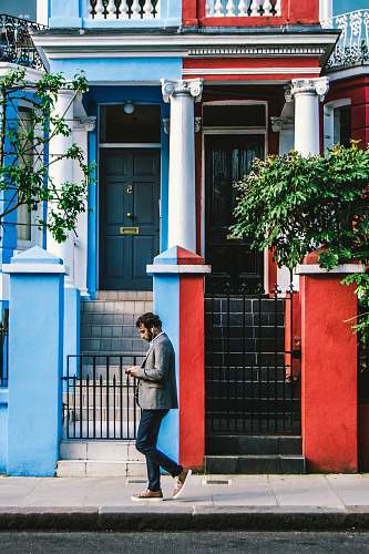 people man using smartphone passing by blue and red houses human