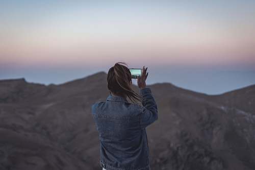human woman in blue denim jacket taking picture of mountain people