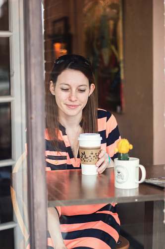 people woman sitting down at table looking at cup in hand cup