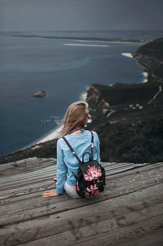people woman sitting on brown plank facing body of water human