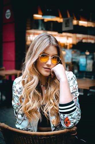 people woman sitting on brown wicker chair holding her face wearing multicolored floral zip-up bomber jacket human
