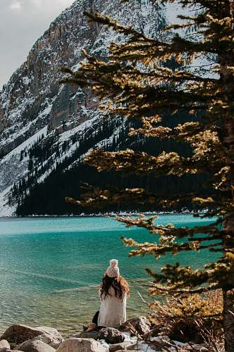 people woman sitting on stone facing body of water and glacier mountain during day human