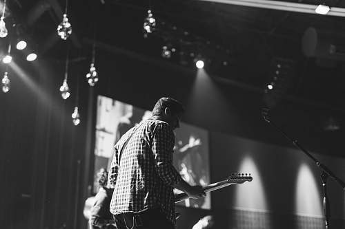 grey grayscale photo of man playing electric guitar stage
