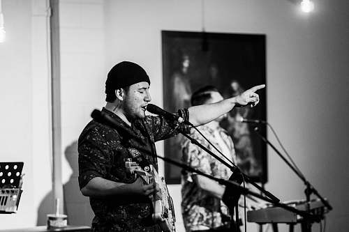 human grayscale photography of singing man playing guitar musical instrument