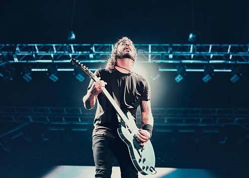 human man playing guitar under stage light struss person