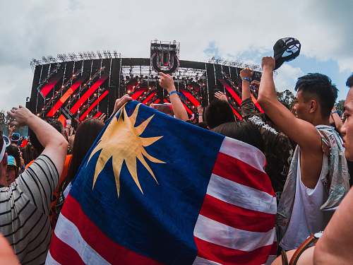 human person holding US flag at crowd under cloudy sky during daytime person