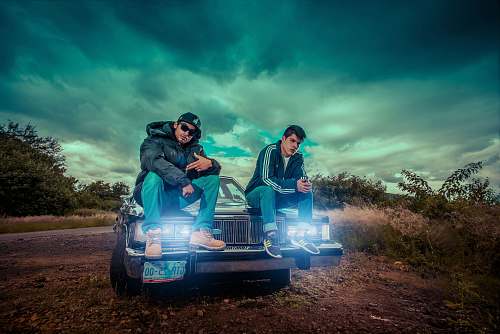 person 2 men sitting on blue car during daytime car