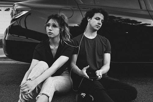person grayscale photo of man and woman leaning on vehicle black-and-white