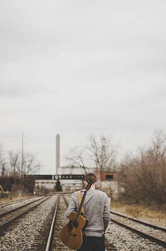 person man carrying guitar walking on train rails people
