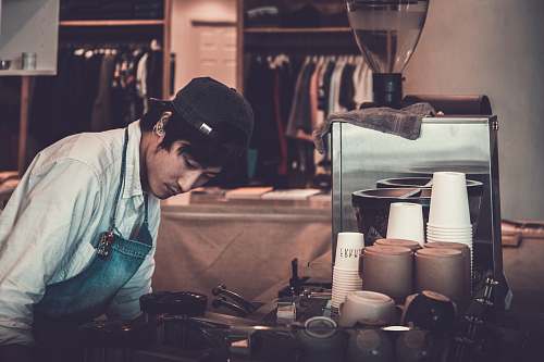 person man facing kitchenware and appliances wearing white top and blue apron people