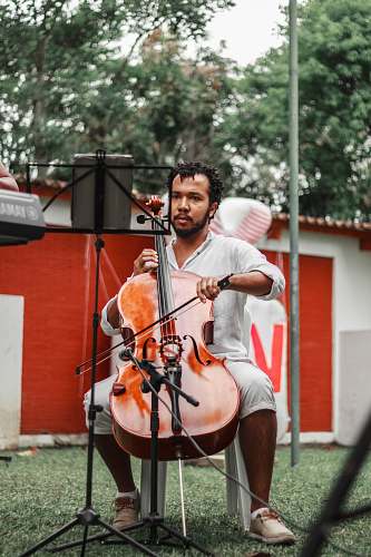 person man holding violin sitting on white plastic chair during daytime musical instrument