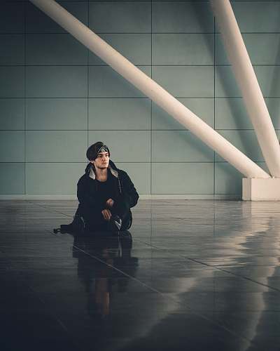 person man in black jacket sitting on brown wooden floor flooring
