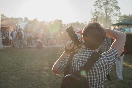 person man in grey and white plaid shirt with backpack and DSLR camera on hand photographer