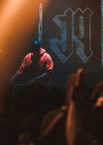 person man in red hoodie with headphones operating DJ mixer machine crowd